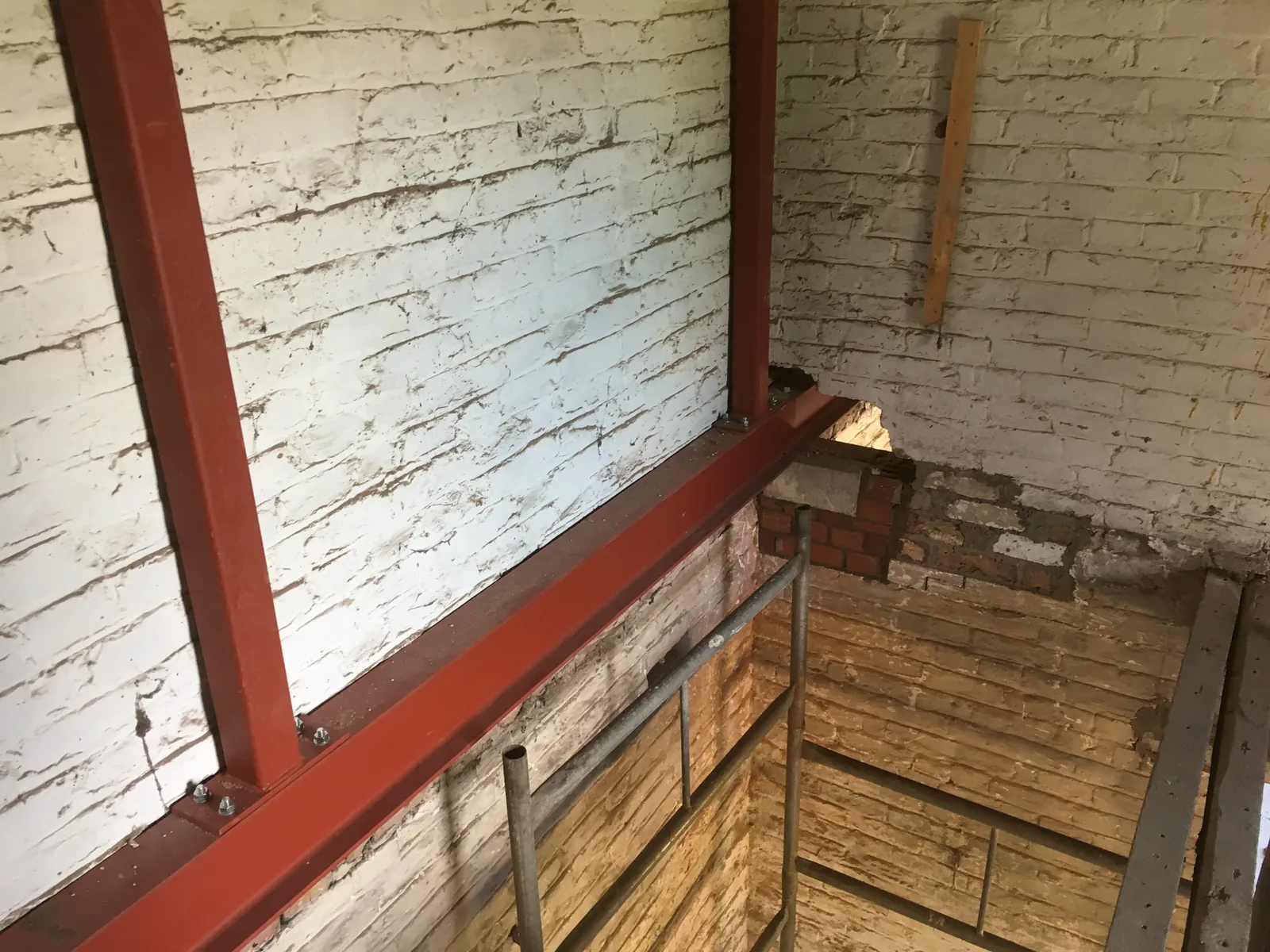 A steel beam let into a whitewashed brick wall with fresh brickwork built up beneath its bearing, seen from a scaffold tower over a new timber floor.