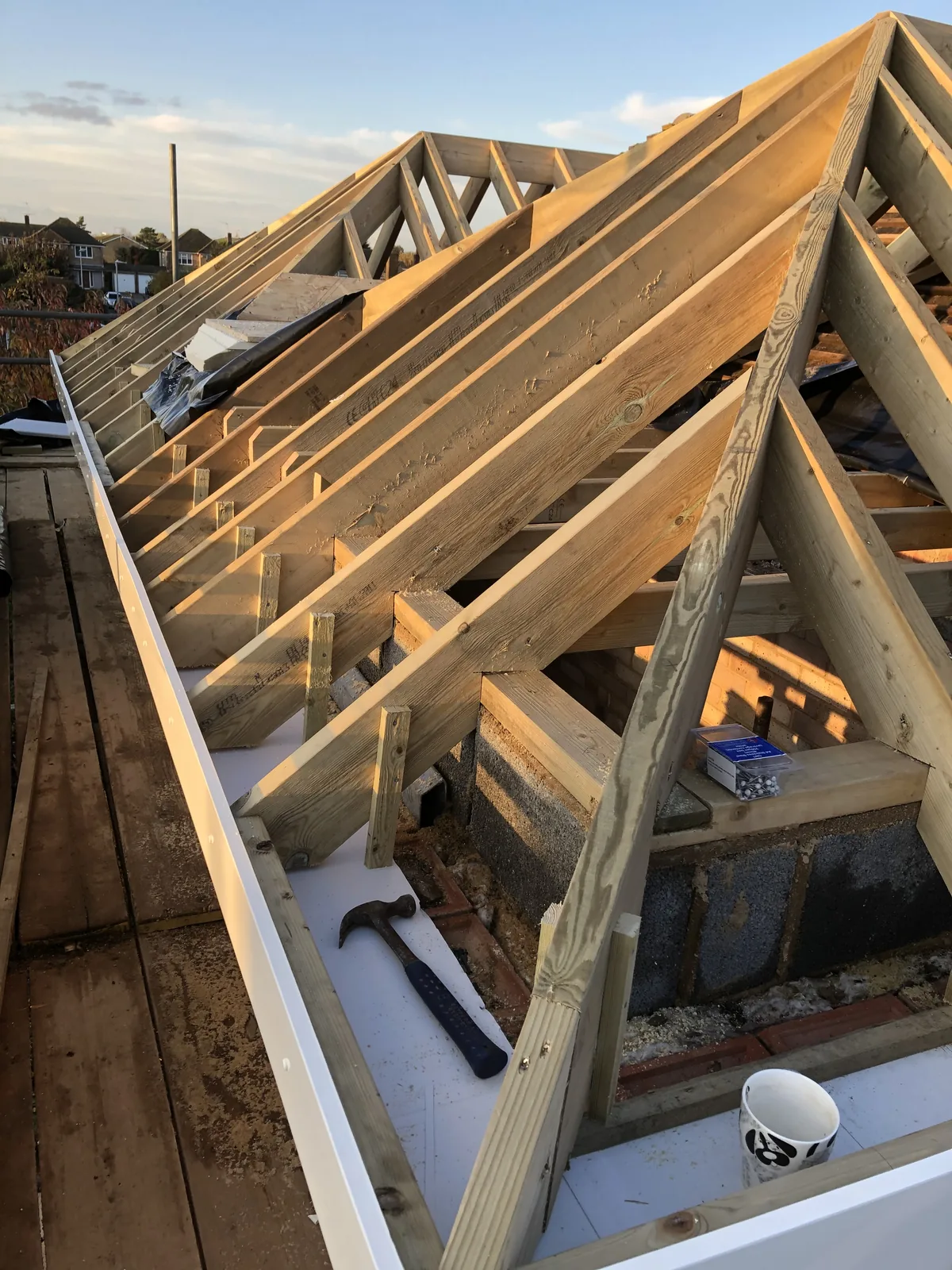 Close view of the new roof frame at the eaves — rafters seated on the wall plate, a hip rafter running up towards the ridge and a new white fascia board fixed along the edge.