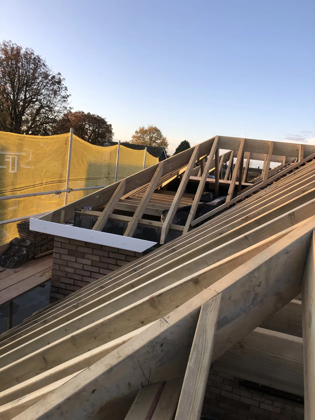 The new roof structure framed up tight against an existing brick chimney stack, with rafters running down to a newly boarded eaves detail.