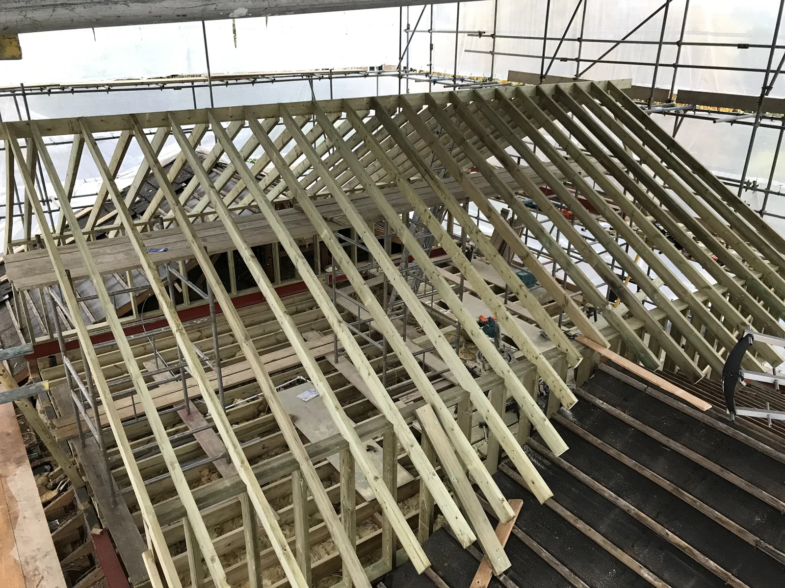 Wide view down onto the finished roof carcass — new rafters spanning the full width of the house inside the scaffold and its protective sheeting.