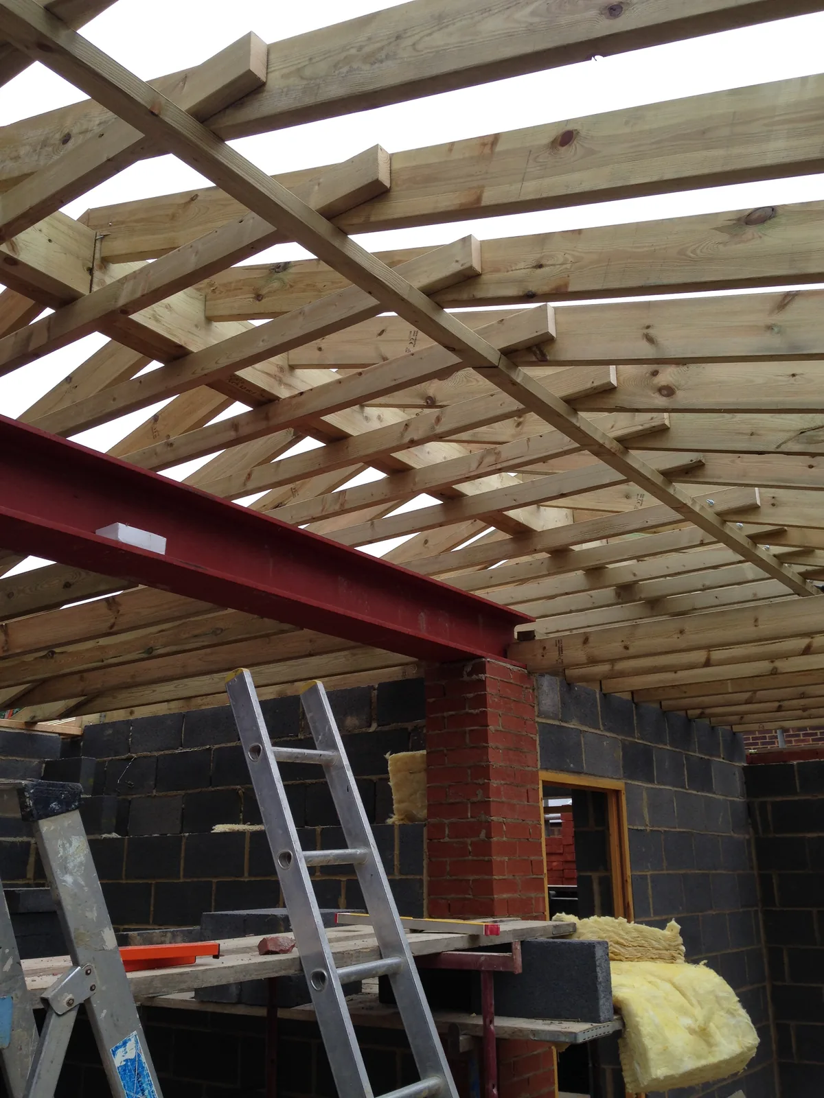 Inside the single-storey range, a red-oxide steel beam spanning the blockwork walls and carrying the ends of the new roof timbers above a brick pier.