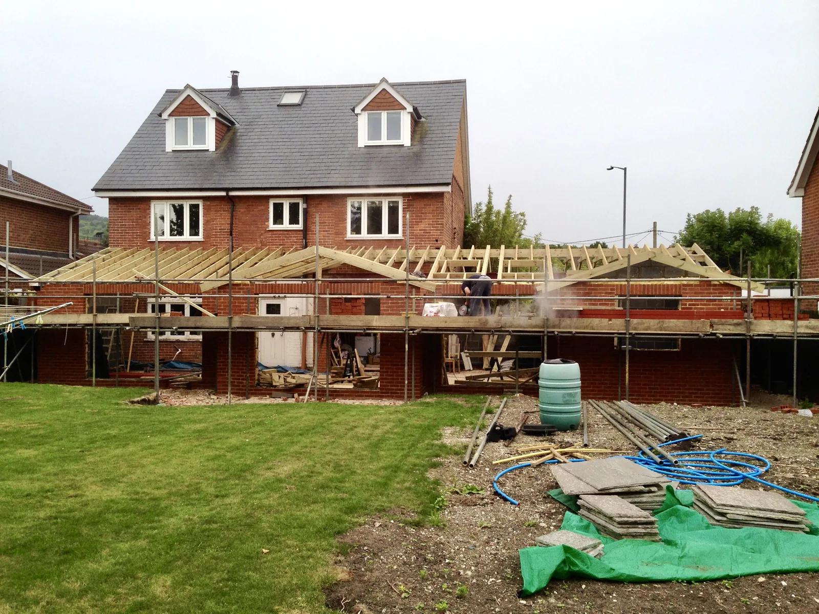 The two-storey brick house complete with slate roof and two dormer windows, with the single-storey rear range in front of it being roofed under a run of scaffold.
