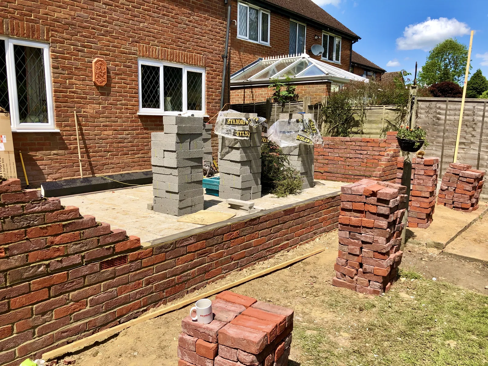 New red brick walls and piers built out from the back of a house to match its existing brickwork, with concrete blocks stacked ready on the prepared ground inside.