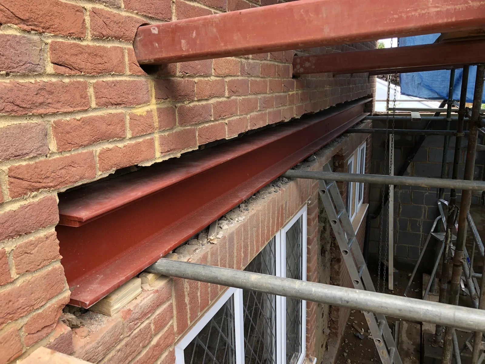 Two red-oxide steel beams let into the existing red brickwork above a ground-floor window, carrying the wall above while the opening below is formed.