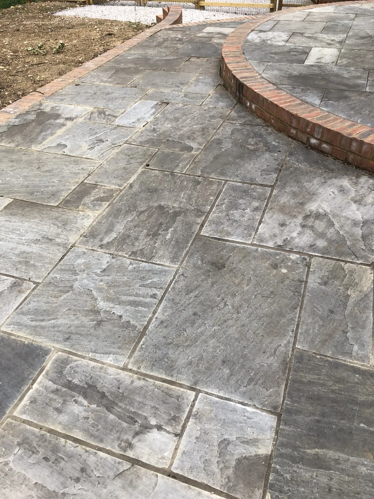 Riven grey natural stone laid in random-coursed sizes, running up to a raised circular terrace edged with a curved brick-on-edge kerb.